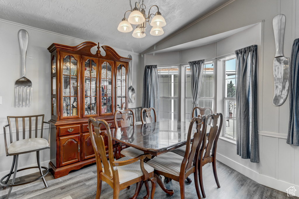 Dining area with light wood-style floors, a chandelier, vaulted ceiling, ornamental molding, and a textured ceiling