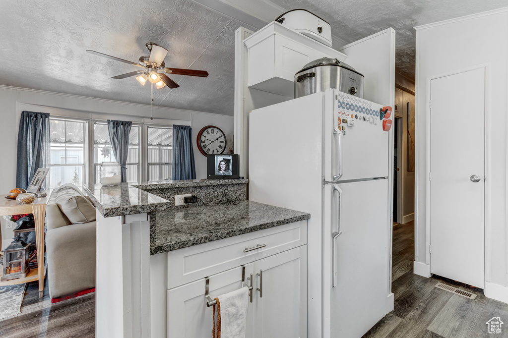 Kitchen with a textured ceiling, freestanding refrigerator, wood finished floors, white cabinets, and a ceiling fan