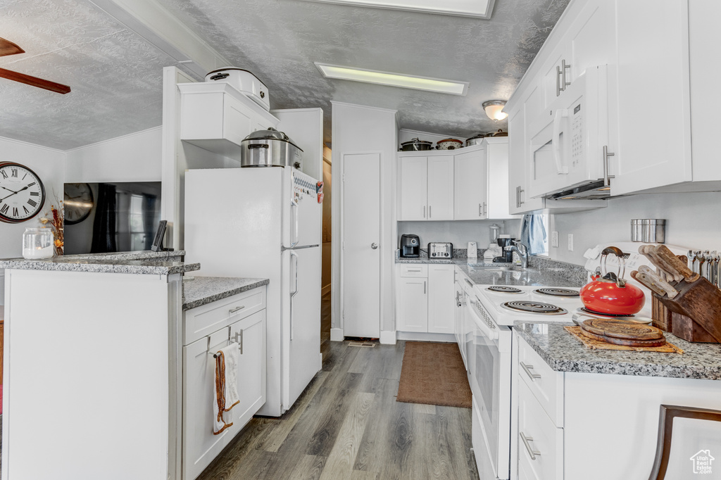Kitchen with white appliances, a textured ceiling, wood finished floors, white cabinets, and light stone countertops
