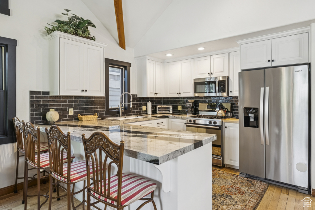 Kitchen featuring appliances with stainless steel finishes, a peninsula, vaulted ceiling, light wood-type flooring, and white cabinets