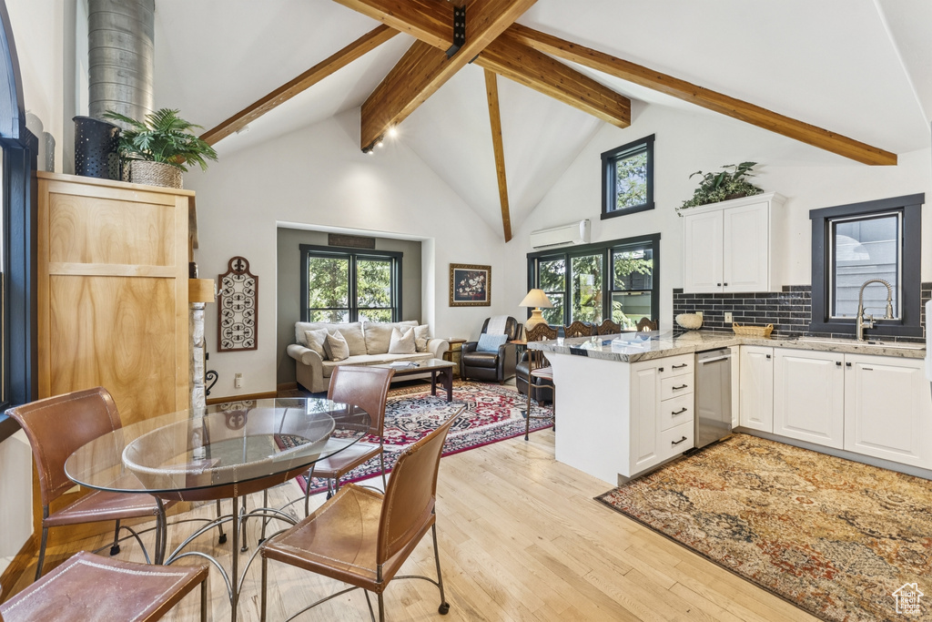 Dining area with beam ceiling, light wood-style flooring, a wall mounted air conditioner, and high vaulted ceiling