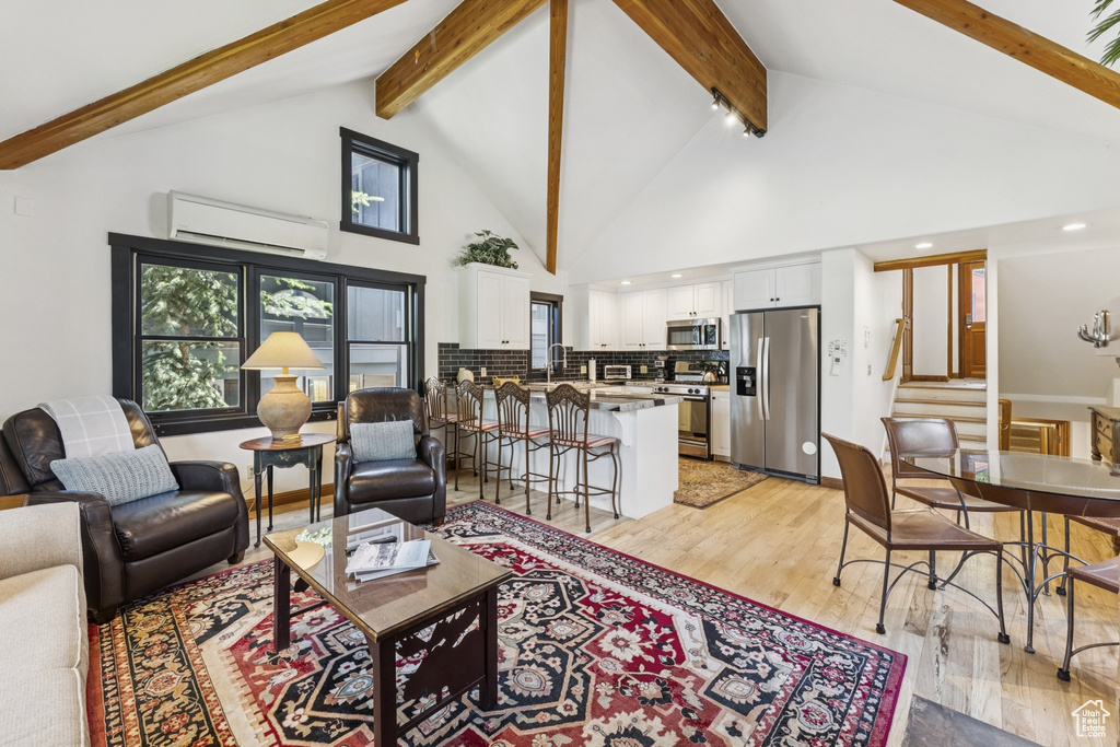 Living room with a wall mounted air conditioner, light wood finished floors, stairway, beamed ceiling, and high vaulted ceiling