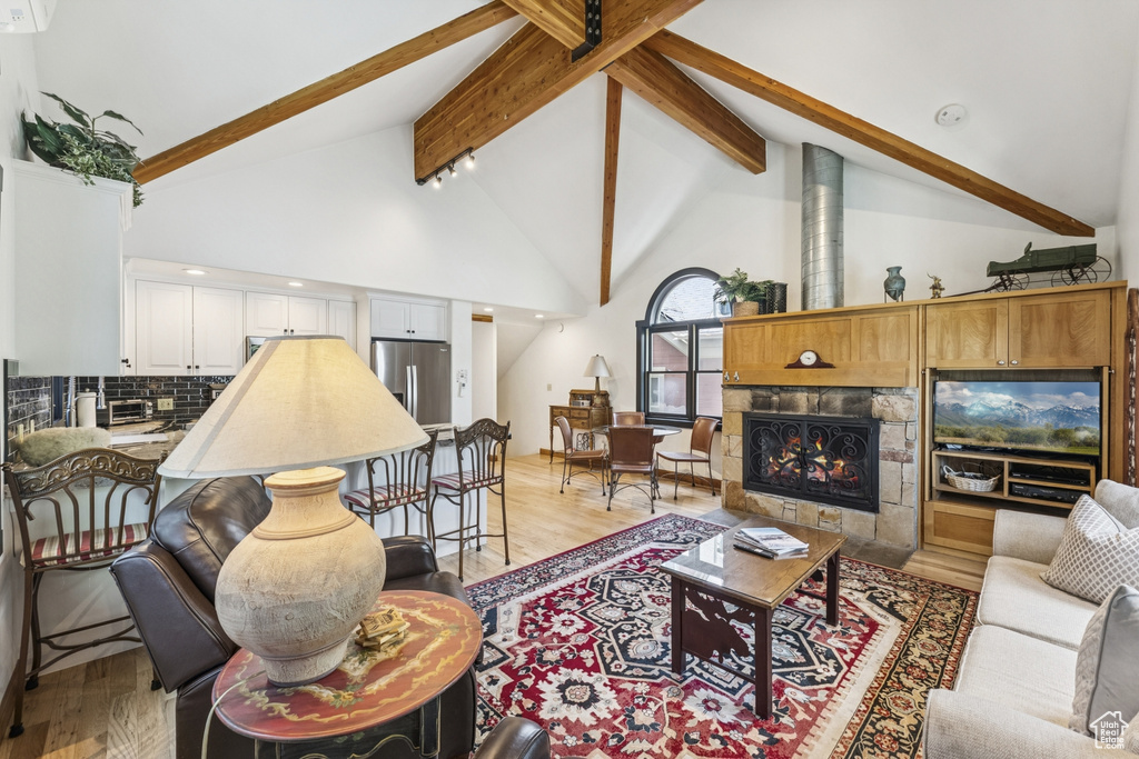 Living room featuring light wood-style flooring, beamed ceiling, high vaulted ceiling, and a fireplace
