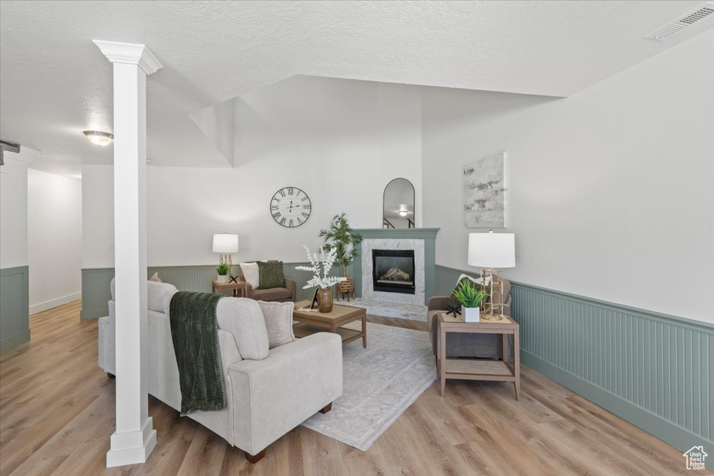 Living area with light wood-style floors, a fireplace, a wainscoted wall, decorative columns, and a textured ceiling