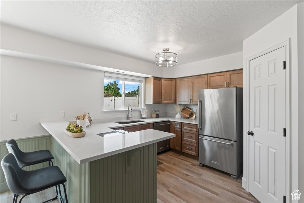Kitchen featuring appliances with stainless steel finishes, a peninsula, light countertops, brown cabinets, and a breakfast bar area