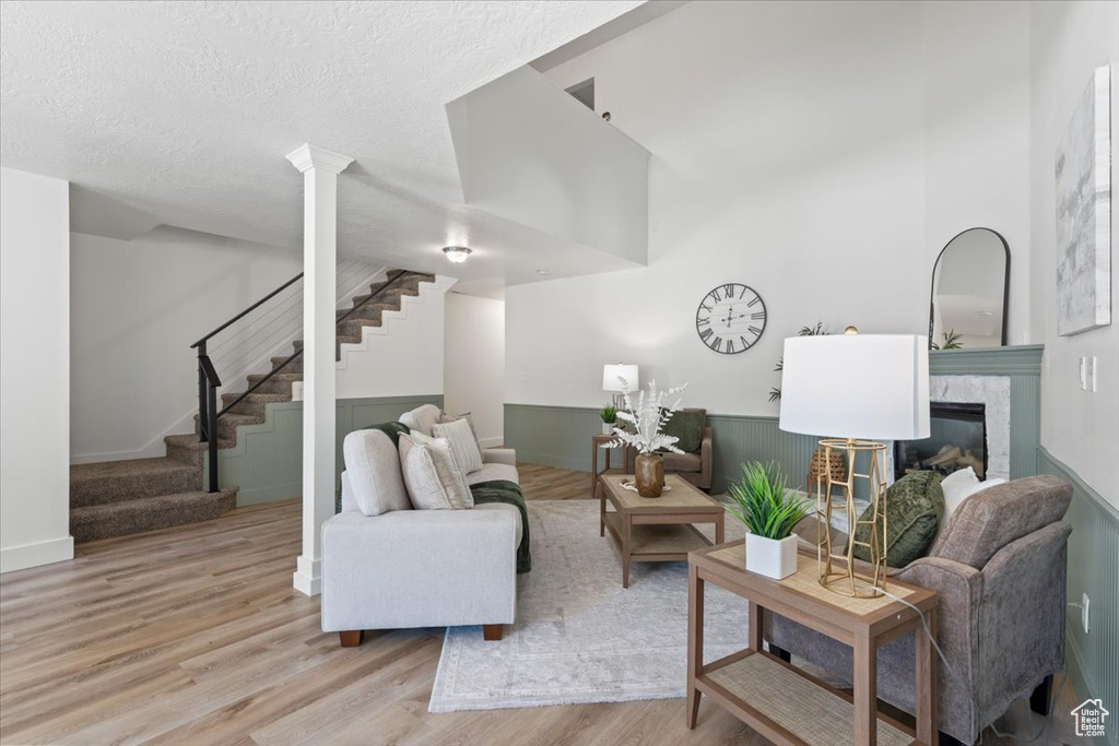 Living area with wood finished floors, stairs, a glass covered fireplace, a wainscoted wall, and a textured ceiling