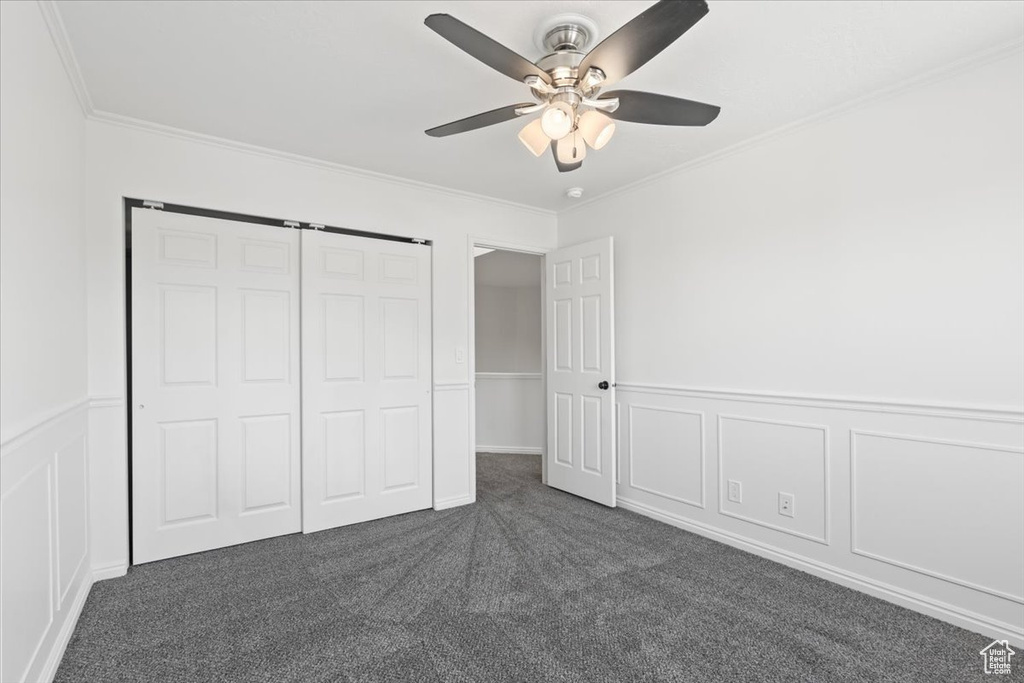 Unfurnished bedroom featuring dark colored carpet, crown molding, a decorative wall, a wainscoted wall, and a ceiling fan