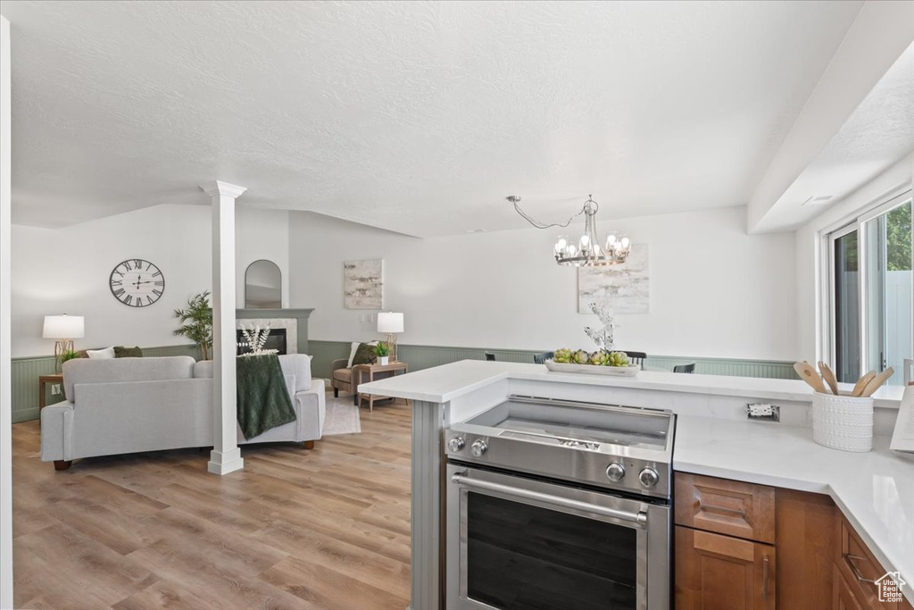 Kitchen with stainless steel electric stove, brown cabinets, light countertops, open floor plan, and light wood-style floors