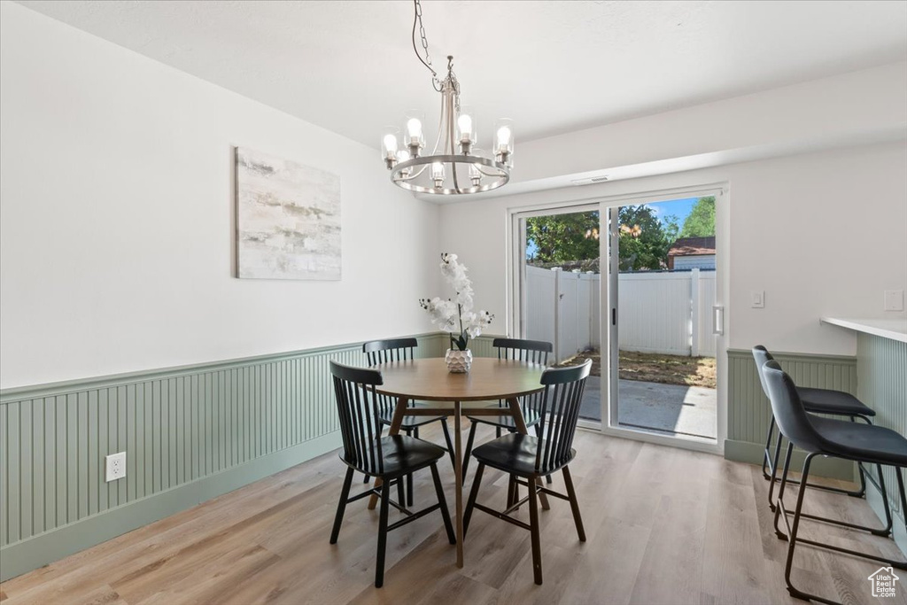 Dining area with a chandelier, a wainscoted wall, and light wood-style flooring