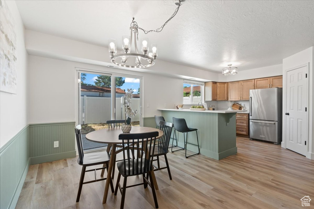 Dining space featuring a chandelier, light wood-style flooring, wainscoting, and a textured ceiling