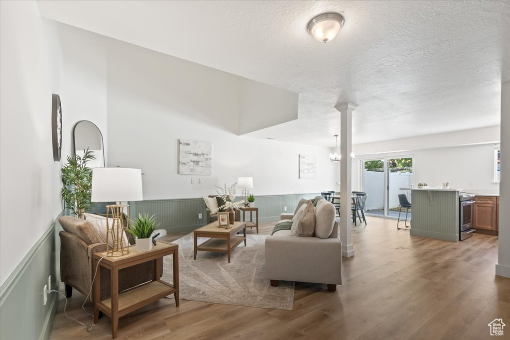 Living room featuring wainscoting, light wood-style floors, ornate columns, and a textured ceiling
