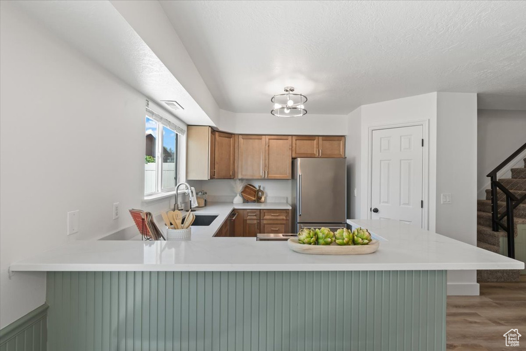 Kitchen with stainless steel fridge, light countertops, a peninsula, and wood finished floors