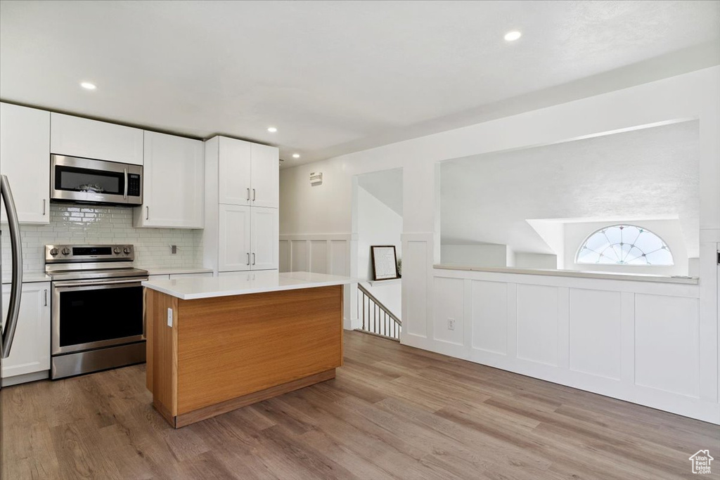 Kitchen featuring appliances with stainless steel finishes, light countertops, a center island, light wood-style flooring, and white cabinetry