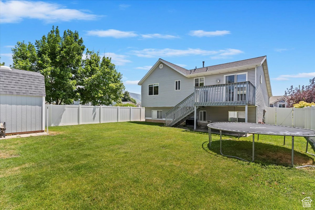 Back of house featuring a trampoline, stairs, a fenced backyard, a deck, and a shed