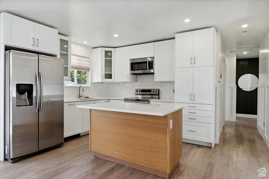 Kitchen featuring appliances with stainless steel finishes, light wood-style floors, tasteful backsplash, white cabinets, and recessed lighting