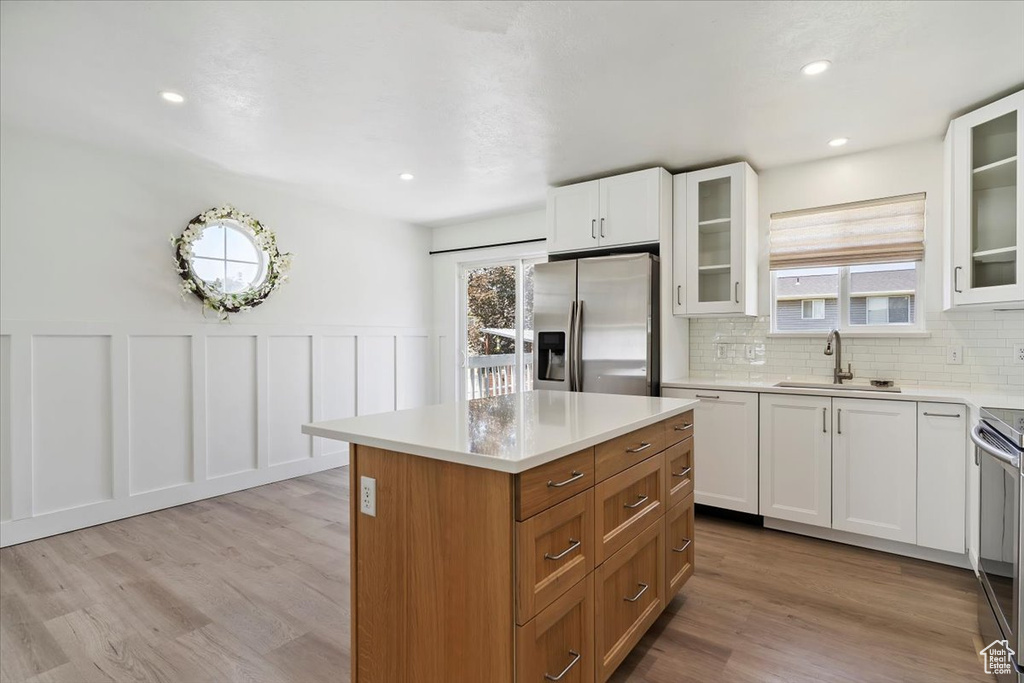 Kitchen featuring appliances with stainless steel finishes, healthy amount of natural light, light wood-style flooring, a kitchen island, and wainscoting