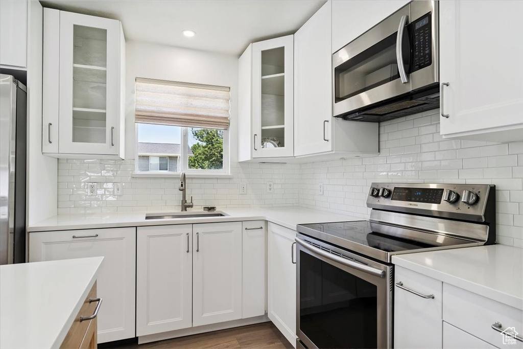 Kitchen with stainless steel appliances, white cabinets, light countertops, decorative backsplash, and recessed lighting