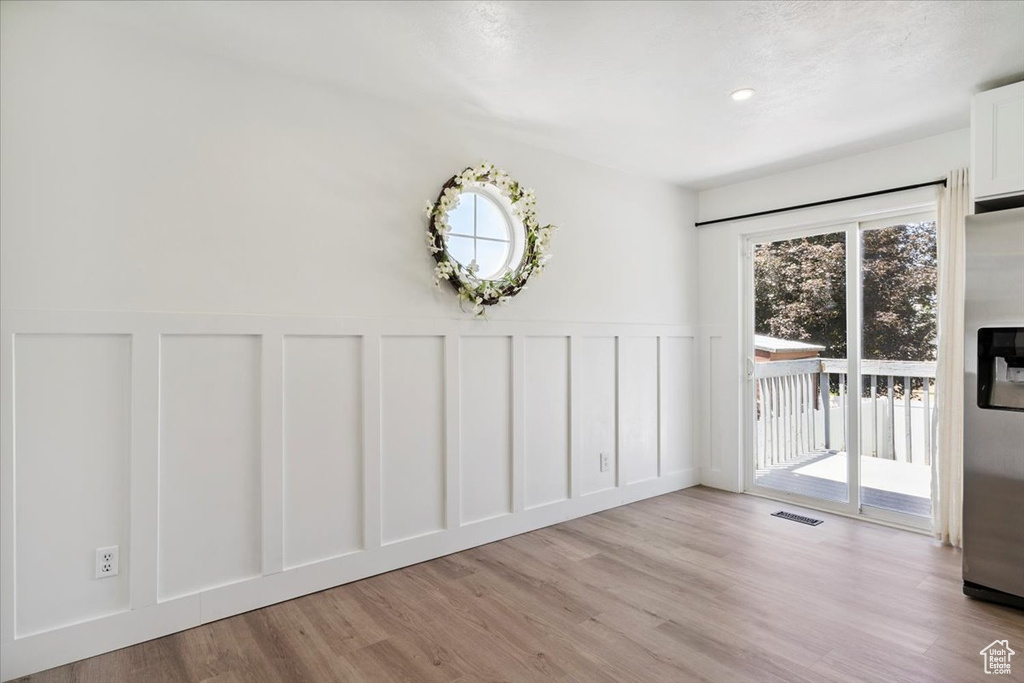 Unfurnished dining area featuring a decorative wall, wainscoting, and light wood-style floors
