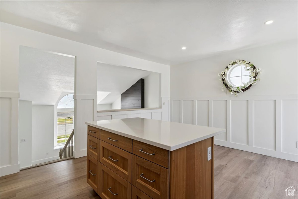 Kitchen with brown cabinets, light wood finished floors, light countertops, a decorative wall, and a center island
