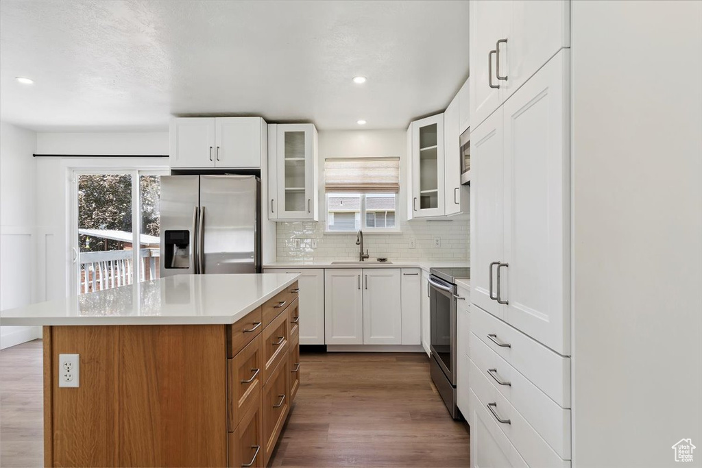 Kitchen featuring stainless steel appliances, a center island, decorative backsplash, glass insert cabinets, and wood finished floors