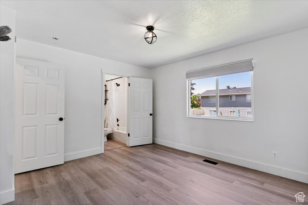 Unfurnished bedroom featuring wood finished floors, connected bathroom, and a textured ceiling