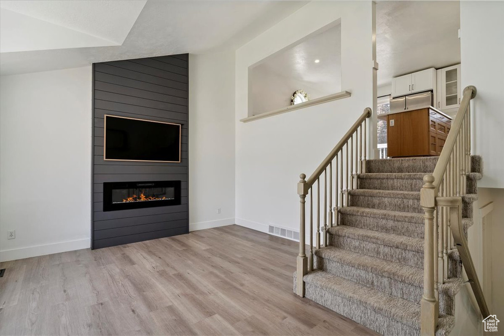 Stairway featuring wood finished floors, a fireplace, and vaulted ceiling