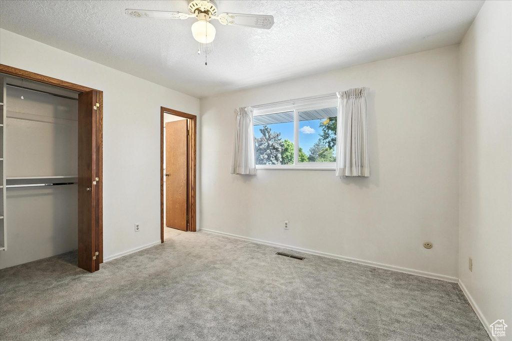 Unfurnished bedroom featuring carpet floors, a textured ceiling, a closet, and ceiling fan