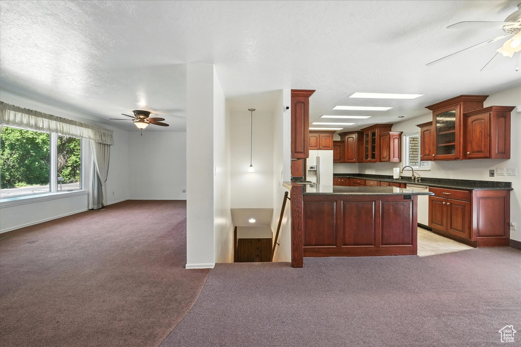Kitchen featuring a ceiling fan, white refrigerator with ice dispenser, light carpet, dark countertops, and a textured ceiling
