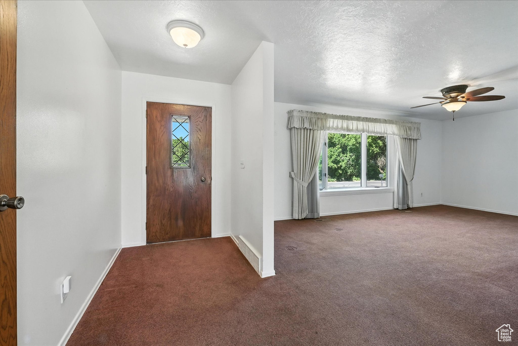 Carpeted entryway with a ceiling fan and a textured ceiling
