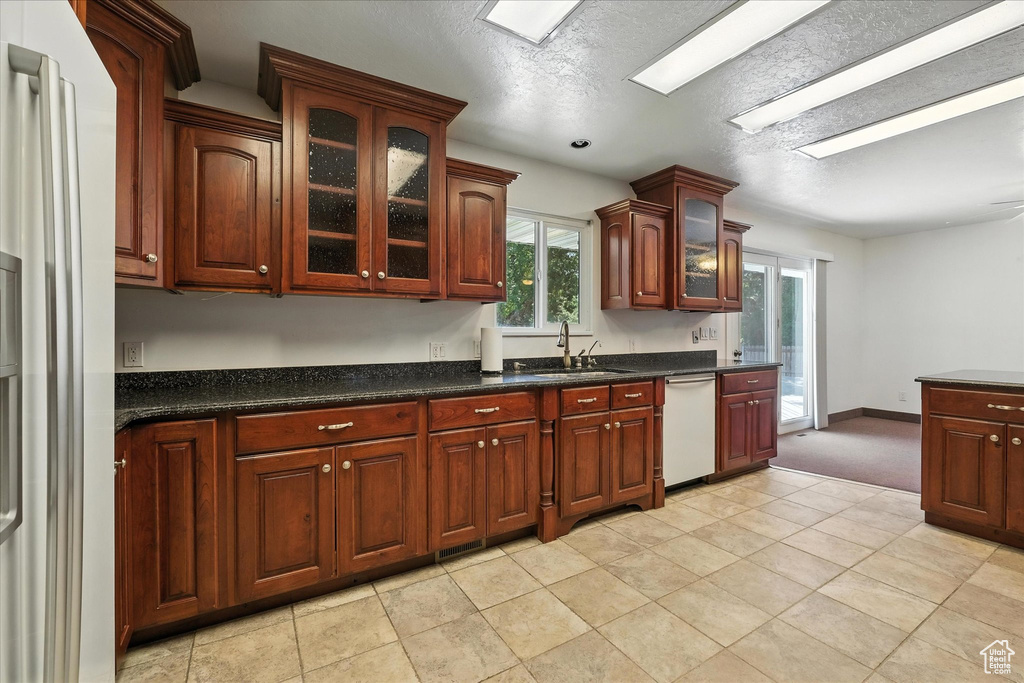 Kitchen featuring dishwasher, refrigerator with ice dispenser, dark countertops, glass insert cabinets, and light colored carpet