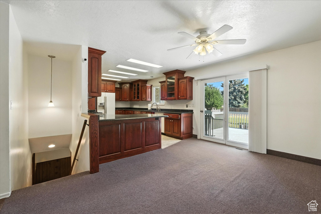 Kitchen with white fridge with ice dispenser, dark countertops, glass insert cabinets, a peninsula, and light colored carpet