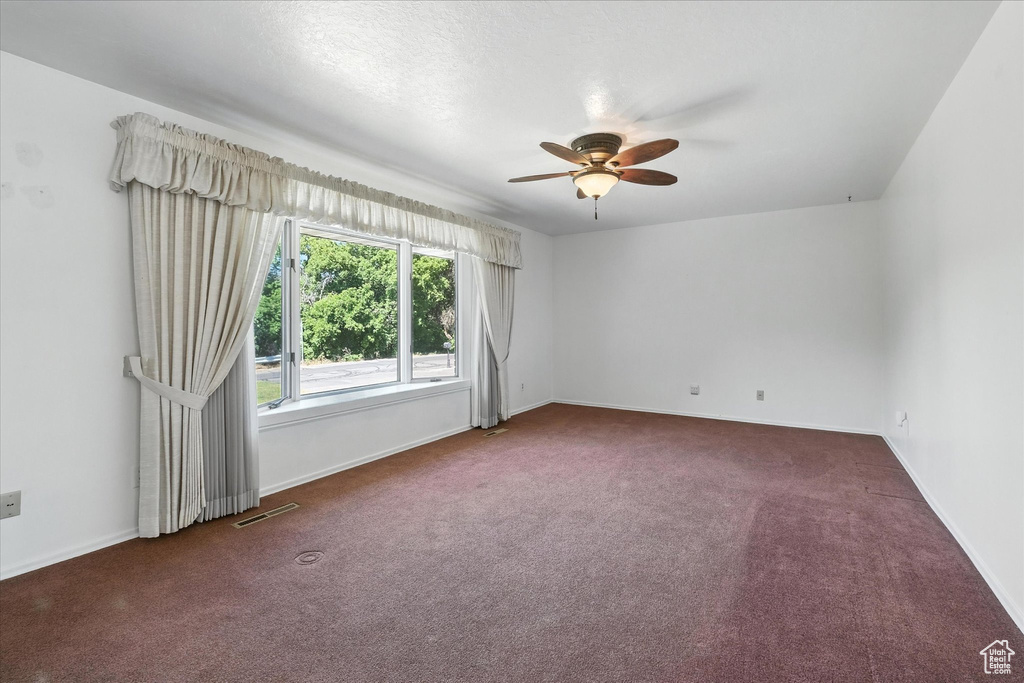 Carpeted empty room featuring ceiling fan and baseboards
