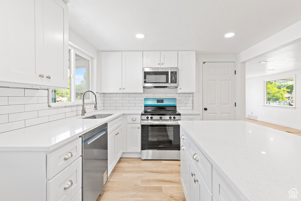 Kitchen with appliances with stainless steel finishes, light wood finished floors, healthy amount of natural light, white cabinetry, and recessed lighting