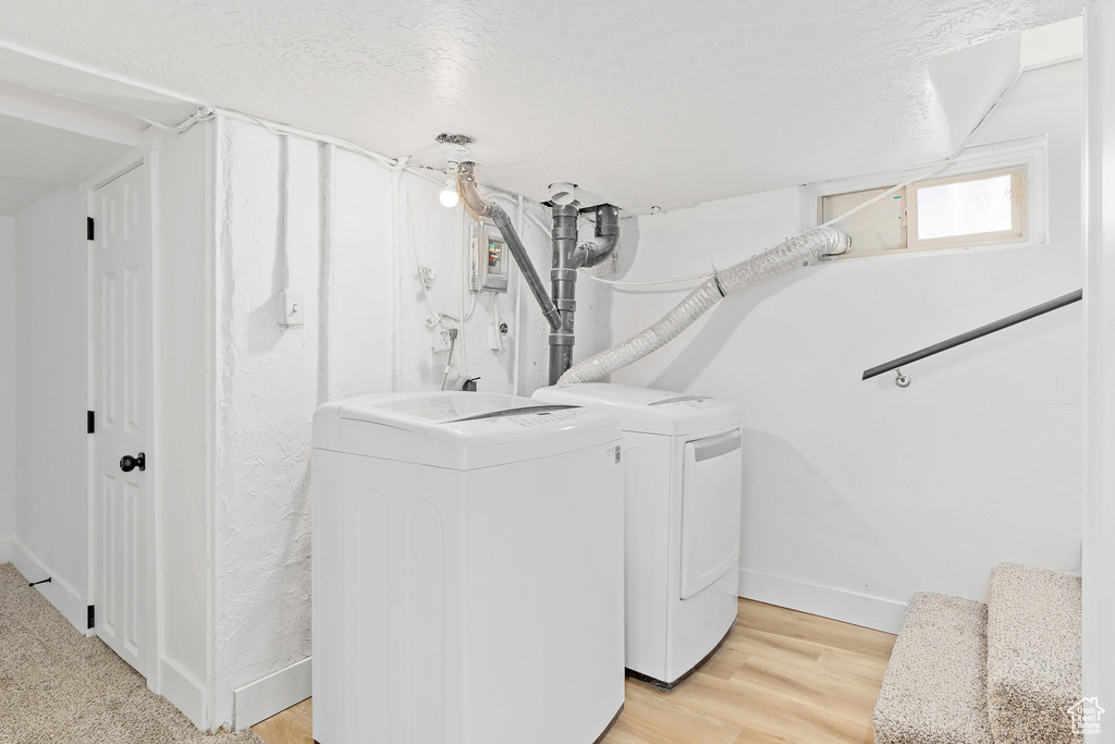 Laundry room with washing machine and clothes dryer, a textured ceiling, and light wood-type flooring