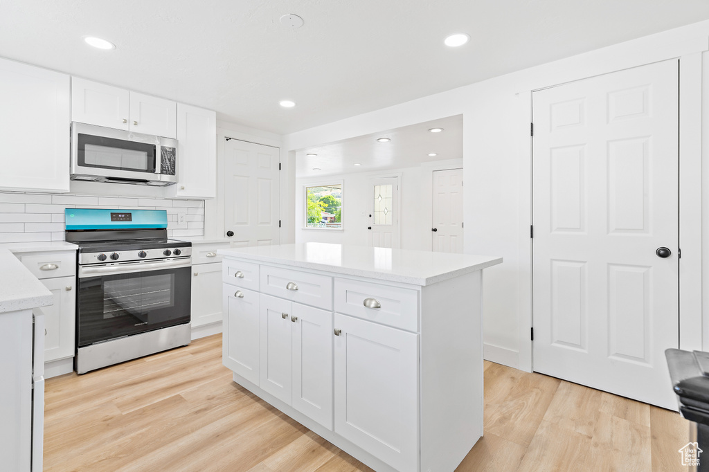 Kitchen with appliances with stainless steel finishes, light wood-style flooring, light countertops, white cabinets, and a kitchen island