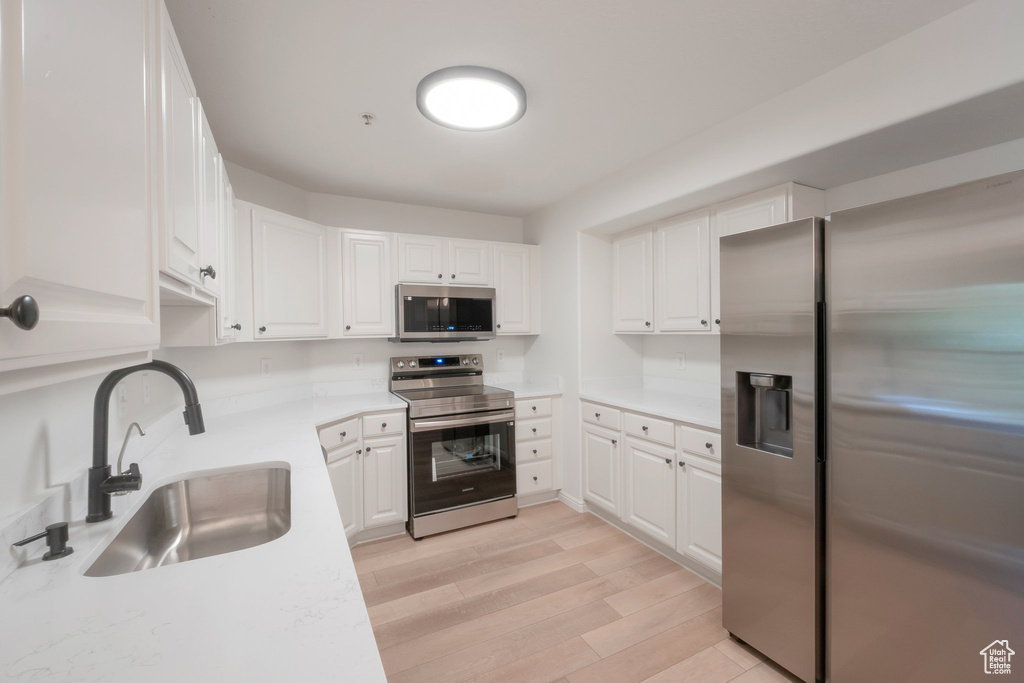 Kitchen featuring appliances with stainless steel finishes, light countertops, white cabinets, and light wood-style flooring