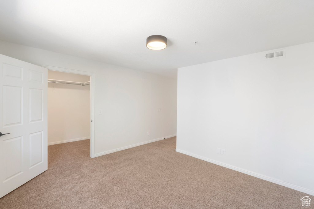 Unfurnished bedroom featuring light carpet, a spacious closet, and a closet