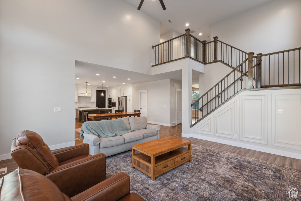 Living room featuring stairs, a high ceiling, wood finished floors, a ceiling fan, and recessed lighting