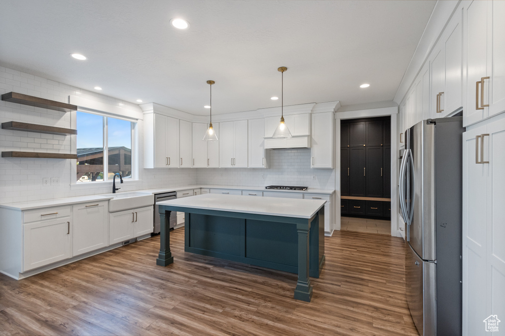 Kitchen featuring appliances with stainless steel finishes, tasteful backsplash, white cabinets, light countertops, and a kitchen island