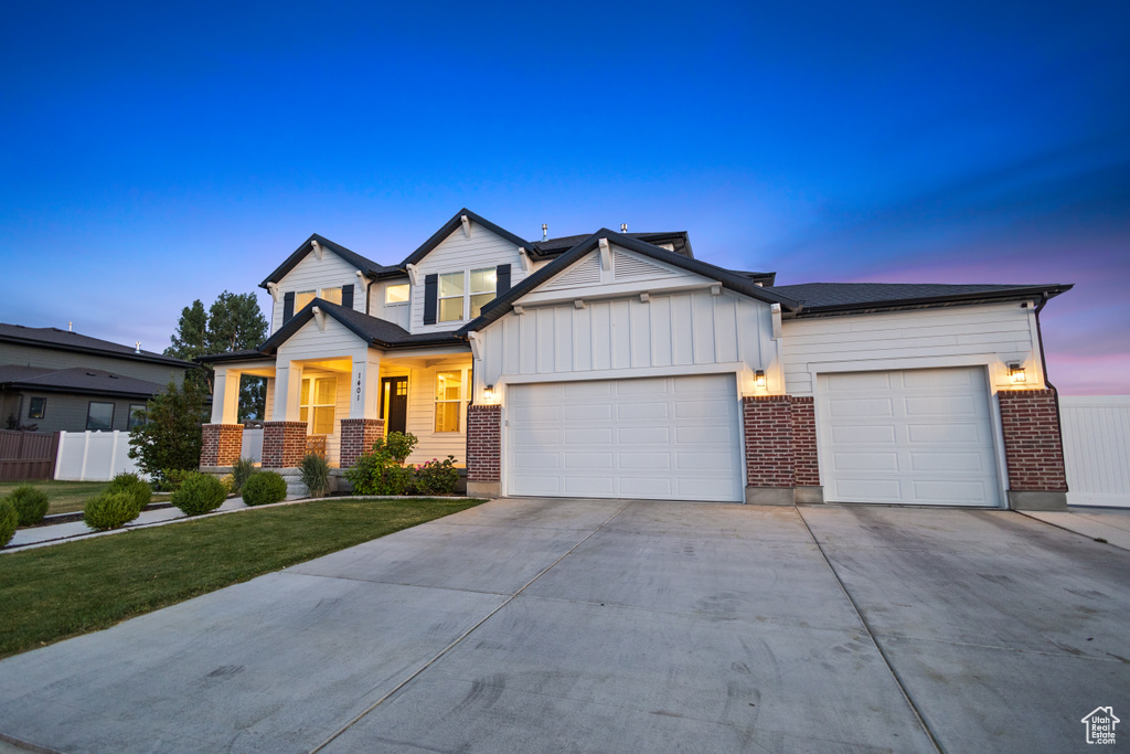 View of front of house with an attached garage, driveway, board and batten siding, brick siding, and covered porch