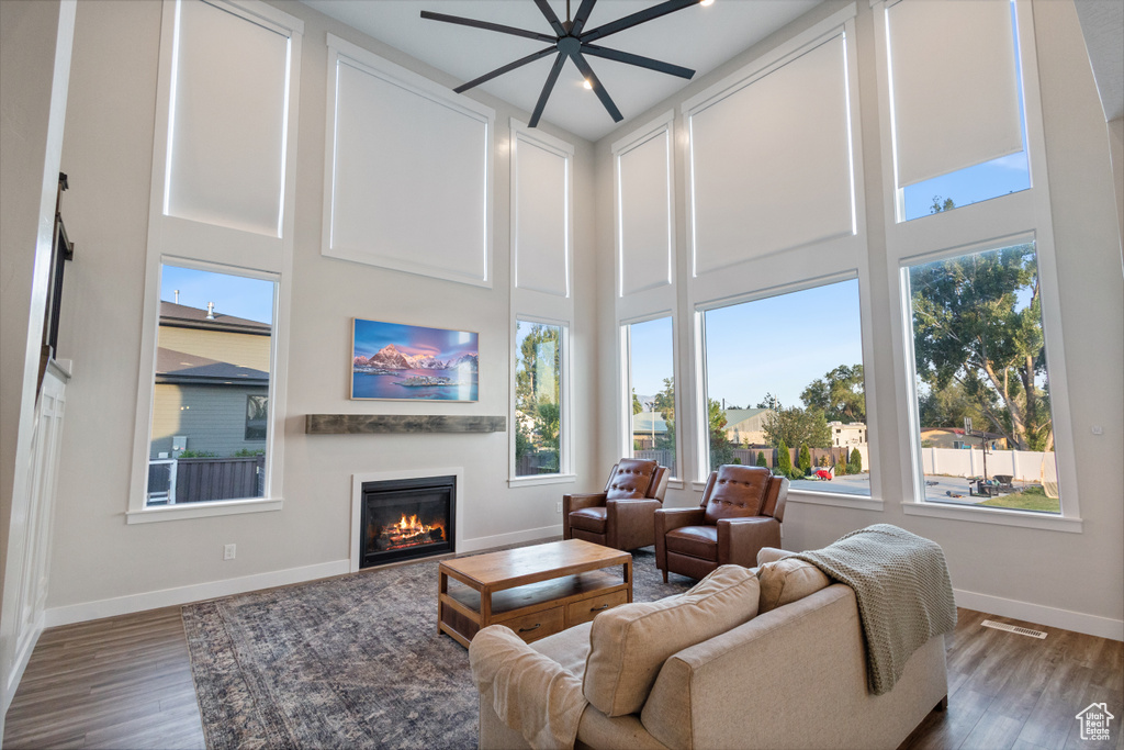 Living room featuring wood finished floors, a glass covered fireplace, ceiling fan, and a high ceiling