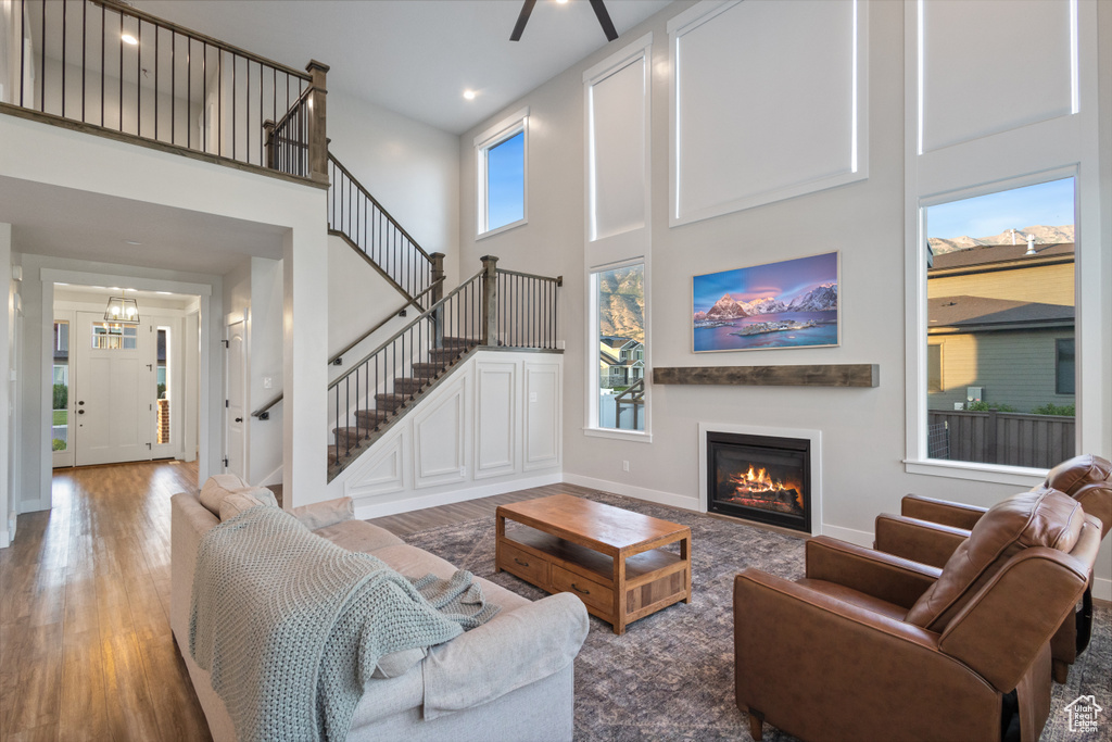 Living room featuring a high ceiling, wood finished floors, a glass covered fireplace, stairway, and a ceiling fan