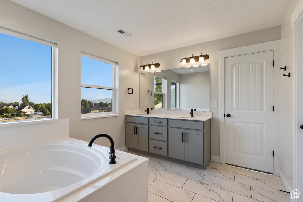 Bathroom with double vanity, a bath, and marble look tile flooring
