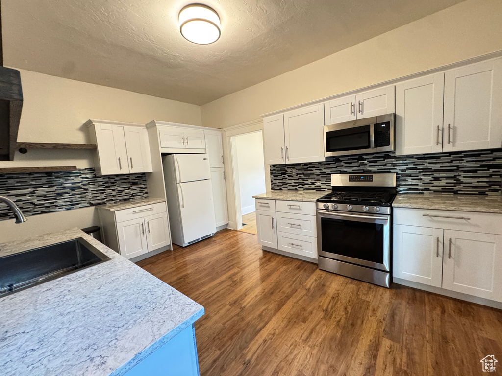 Kitchen with appliances with stainless steel finishes, backsplash, white cabinets, dark wood-type flooring, and a textured ceiling