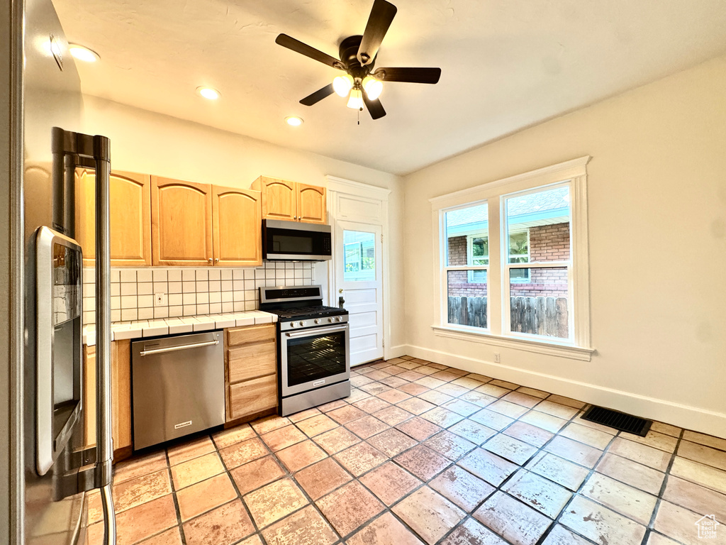 Kitchen with stainless steel appliances, tile countertops, light brown cabinets, tasteful backsplash, and a ceiling fan