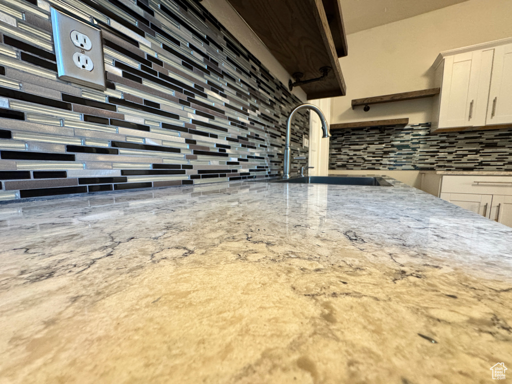 Kitchen view of tasteful backsplash, white cabinetry, and light stone countertops