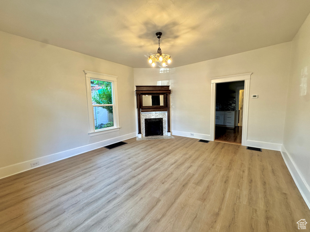 Unfurnished living room with a chandelier, a fireplace, and light wood-type flooring