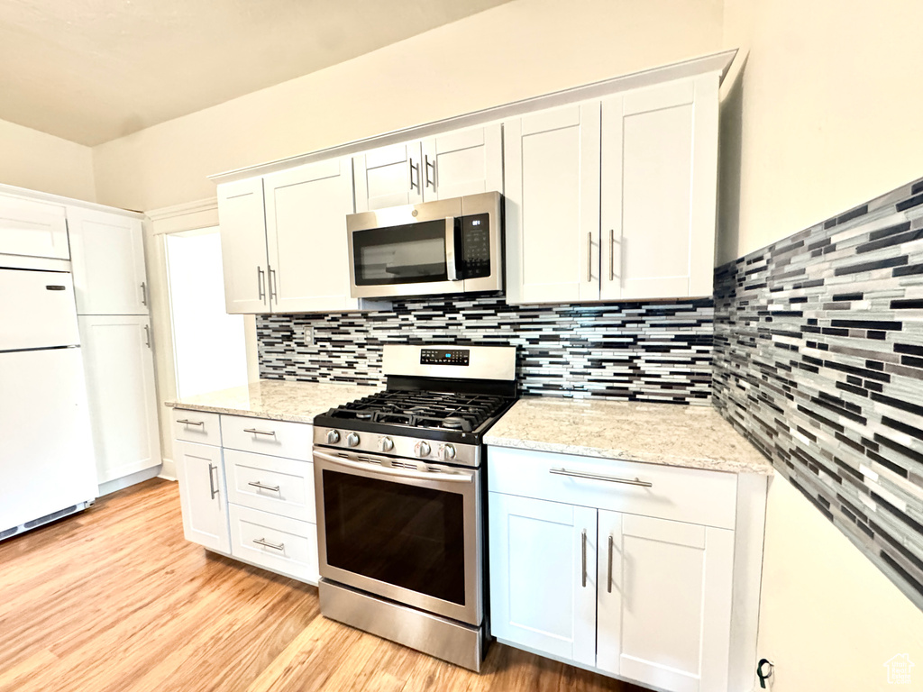 Kitchen with appliances with stainless steel finishes, decorative backsplash, light wood-type flooring, and white cabinetry