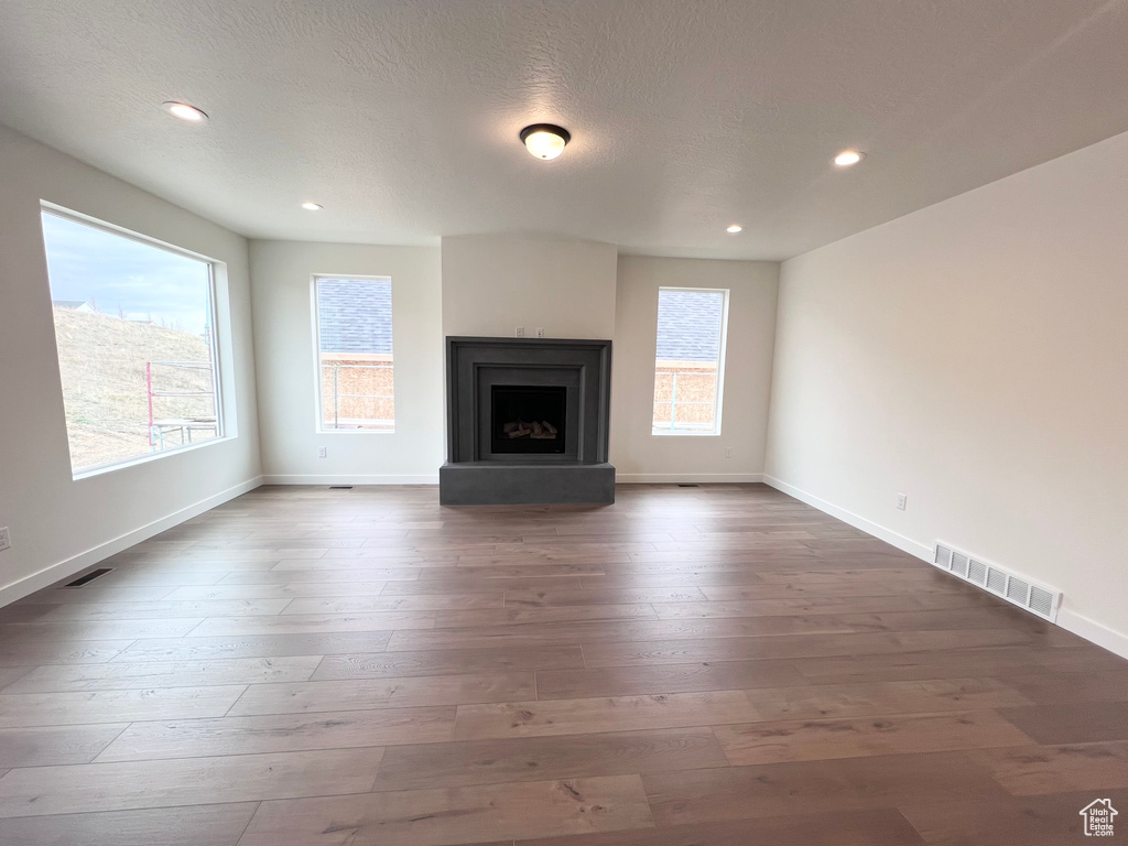 Unfurnished living room with dark wood-style flooring, recessed lighting, a fireplace with raised hearth, and a textured ceiling