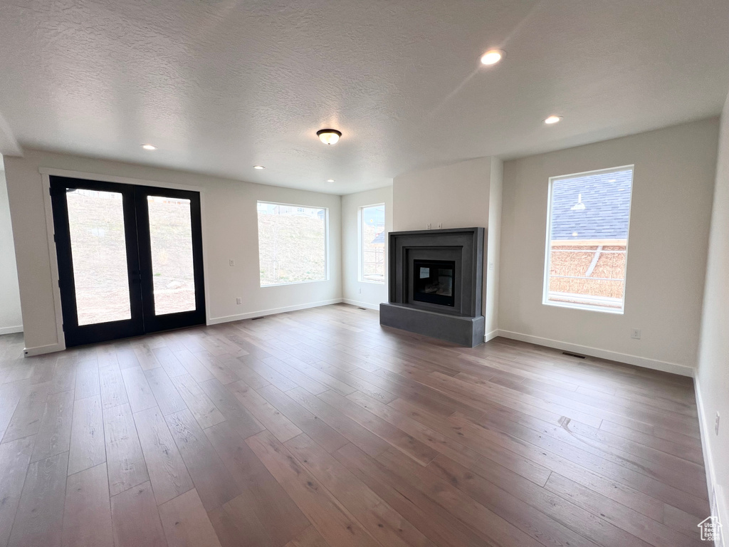 Unfurnished living room with french doors, recessed lighting, wood-type flooring, a glass covered fireplace, and a textured ceiling